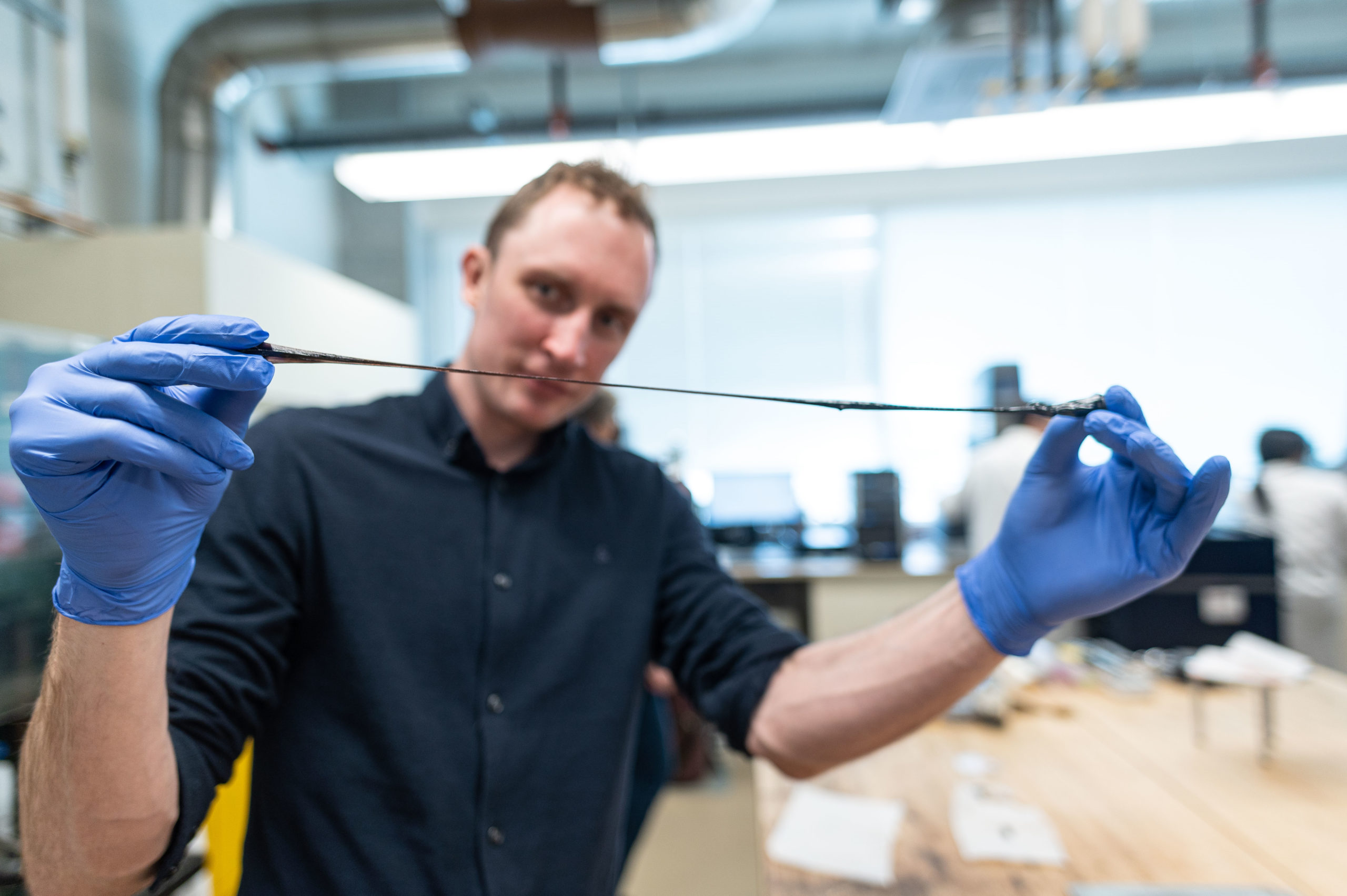 man in blue latex gloves stretches a dark strand of polymer 