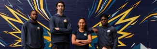 A group of athletic-looking students pose in navy blue UBC-branded athletic gear, in front of a navy blue brick wall.