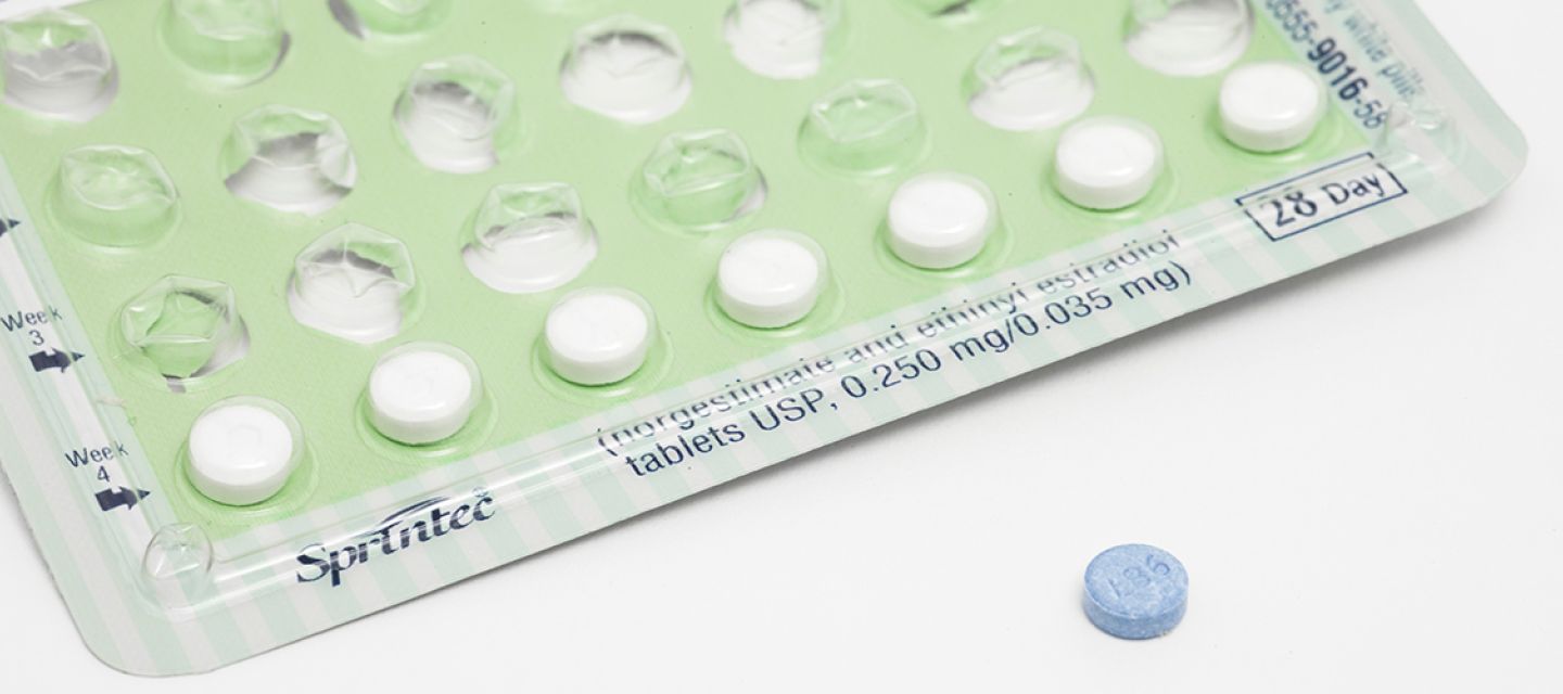 A mostly empty packet of birth control pills, with one blue pill out of the packet and on the table surface.
