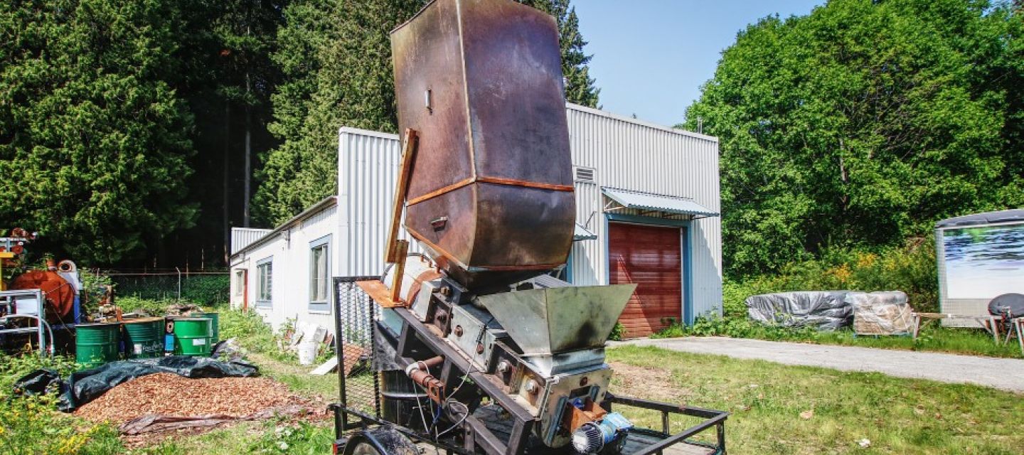 This small, mobile bioreactor turns forestry or agricultural waste. It is pictured in a grassy field with treed area behind and is a rusty metal-based contraption.