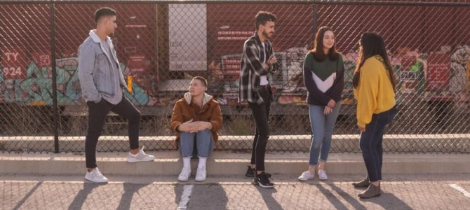 Photo of 5 young adults standing in an industrial area, in front of a chain link fence, copyright by Eliott Reyna on Unsplash