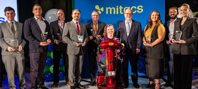group photo of award winners and Mitacs representatives in front of a blue banner with yellow Mitacs logo on it
